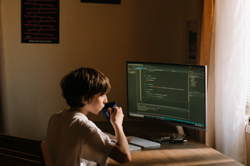 Person coding in front of a large monitor, sipping coffee.